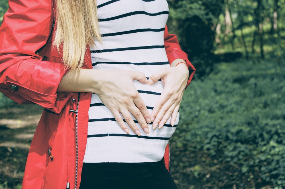 woman holding her hands in heart shape over her pregnant abdomen